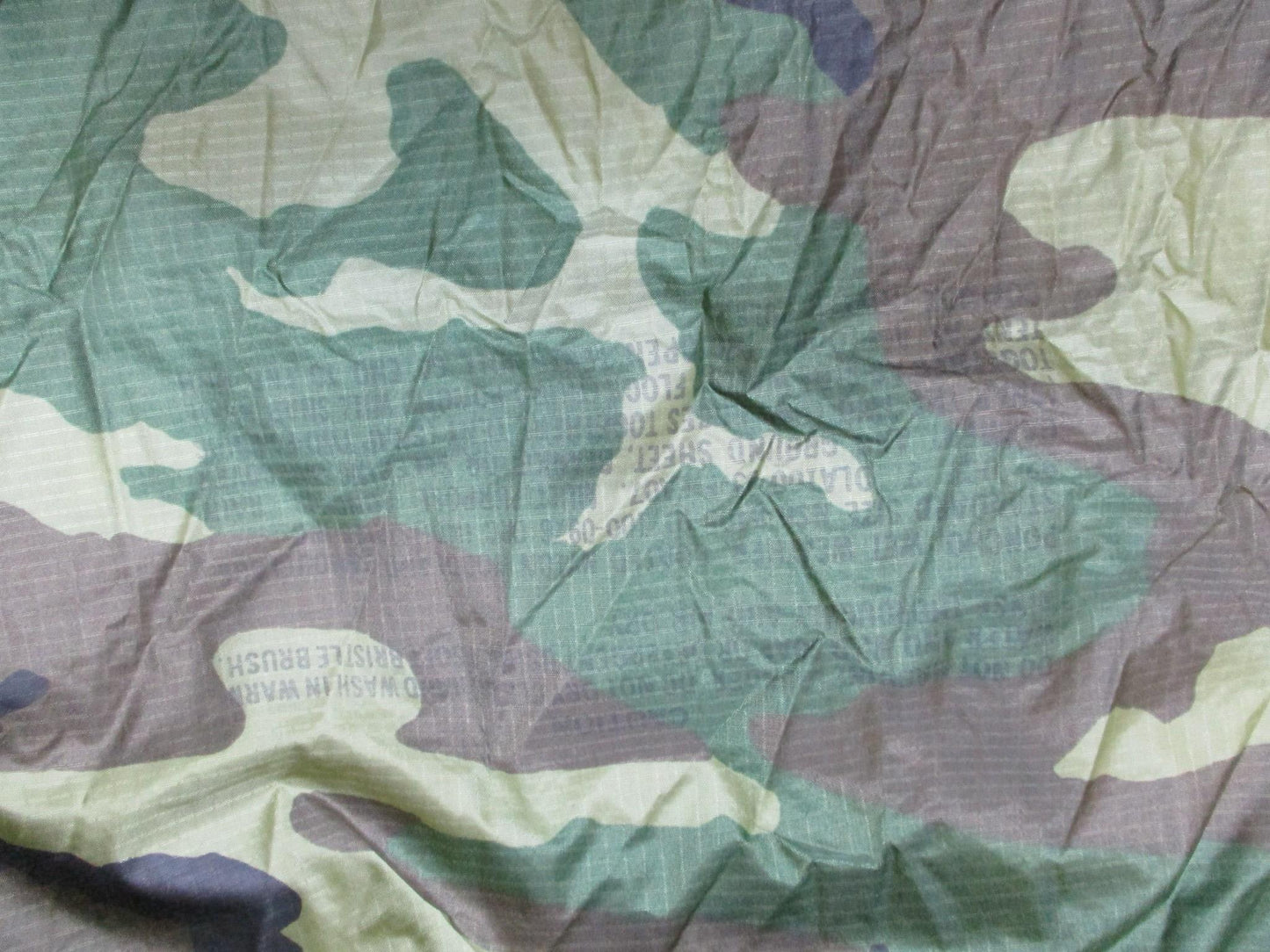 USGI military rain poncho in woodland camouflage, made of durable ripstop fabric, worn by soldiers for weather protection.